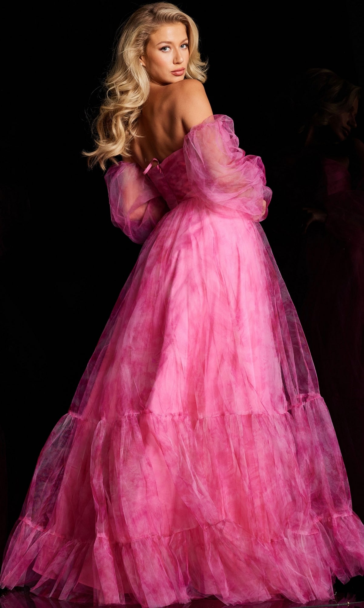 A woman with long blonde hair poses against a black background wearing the Jovani Long-Sleeve Long Pink Formal Dress 38605.